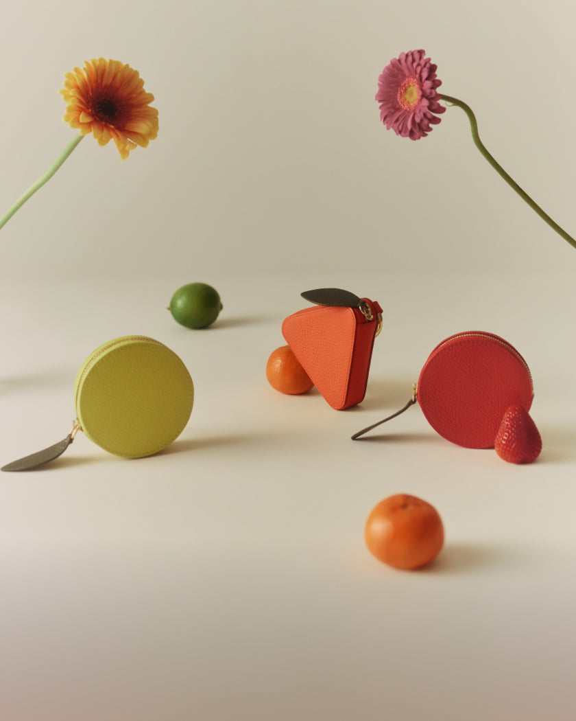 Three fruit-shaped coin purses are placed beside fruits and flowers.