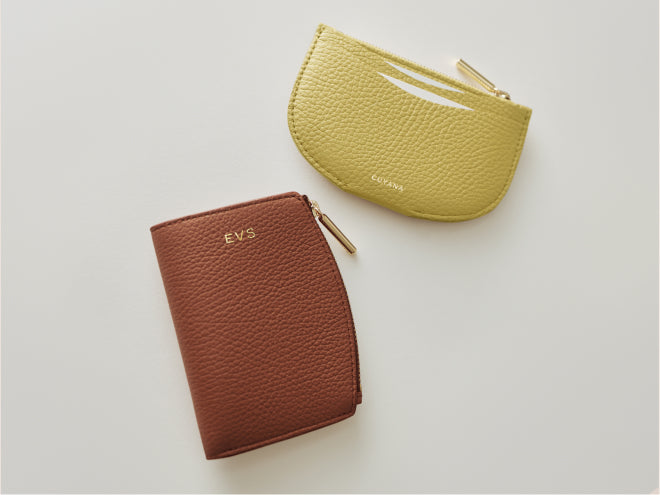 Two textured wallets, one rectangular and one semi-circular, with zippers on a plain surface.