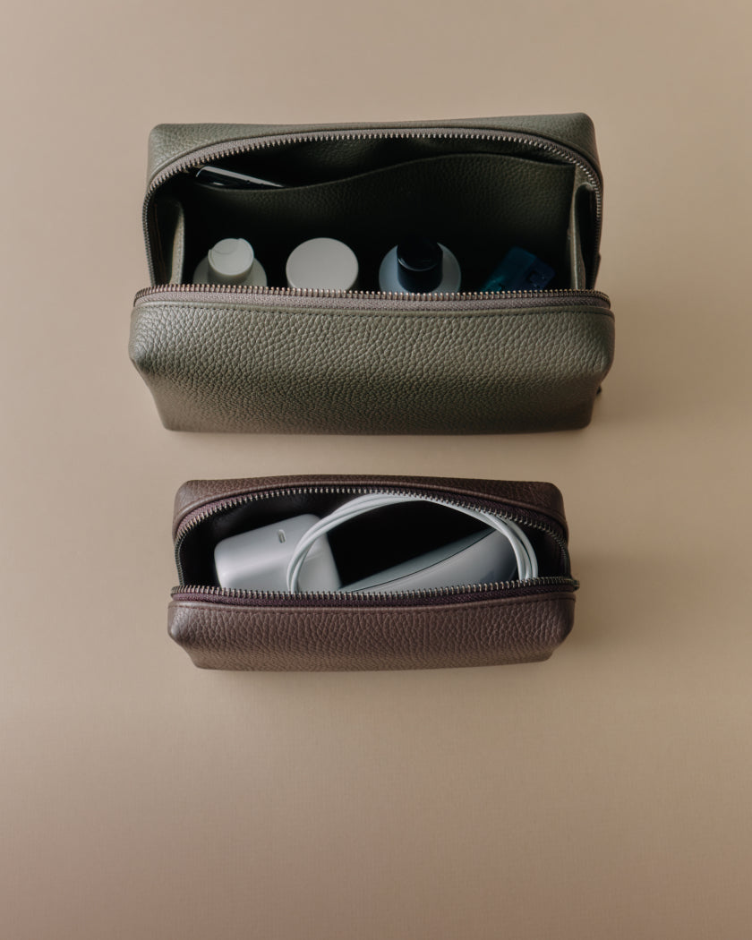 Two leather toiletry bags with items inside on a flat surface.