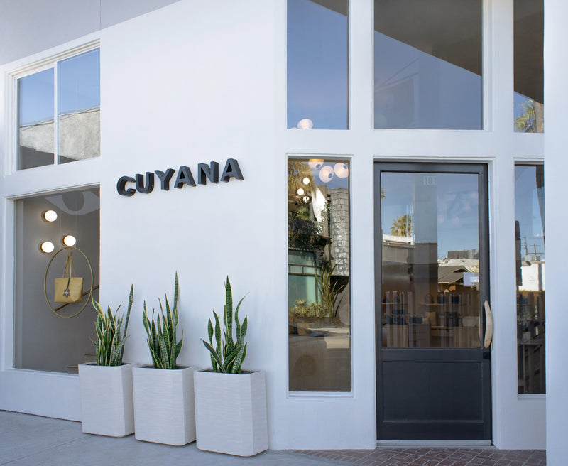 Storefront with Cuyana sign, large windows, and potted plants at entrance.