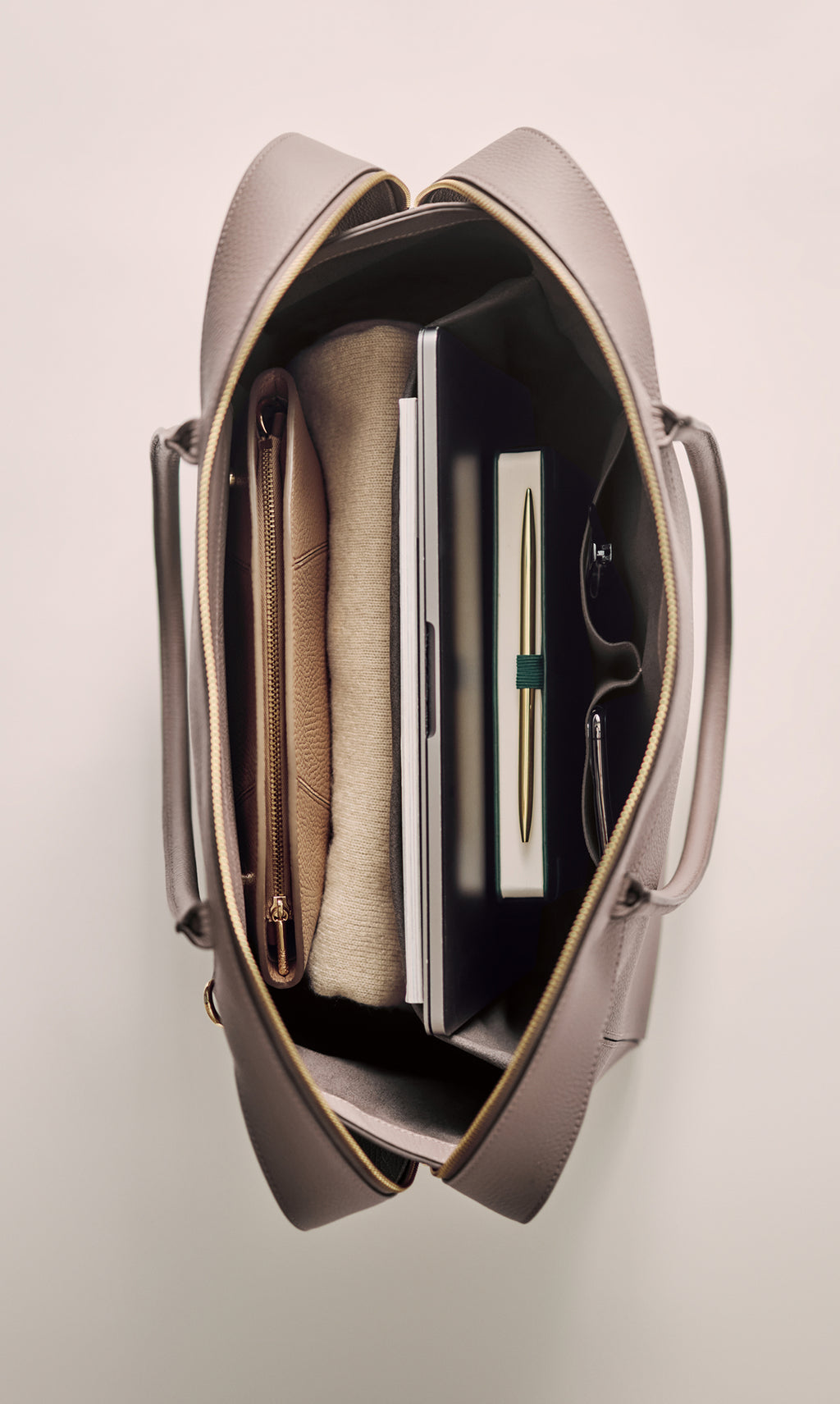 Open travel bag with a pen, book, pouch, and tablet neatly organized inside.