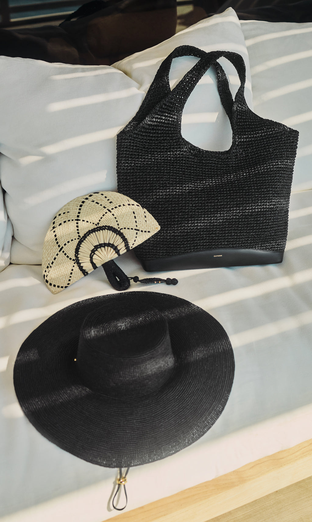 Woven bag, bamboo handheld fan, and wide-brimmed hat on fabric background