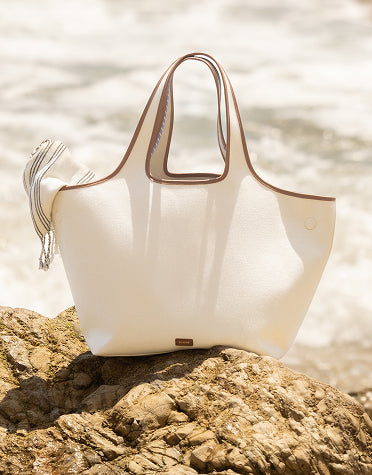 Beach bag on a rock near the shore with a cloth peeking out of it.