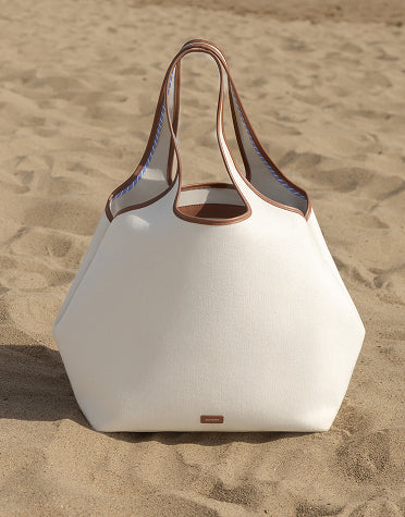 A large tote bag sits on a sandy beach.