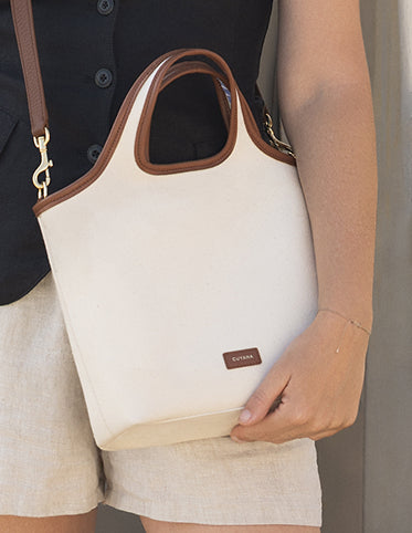 Person holding a handbag with a shoulder strap and wearing shorts.