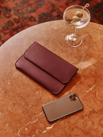 Envelope clutch, cocktail glass, and smartphone on round table