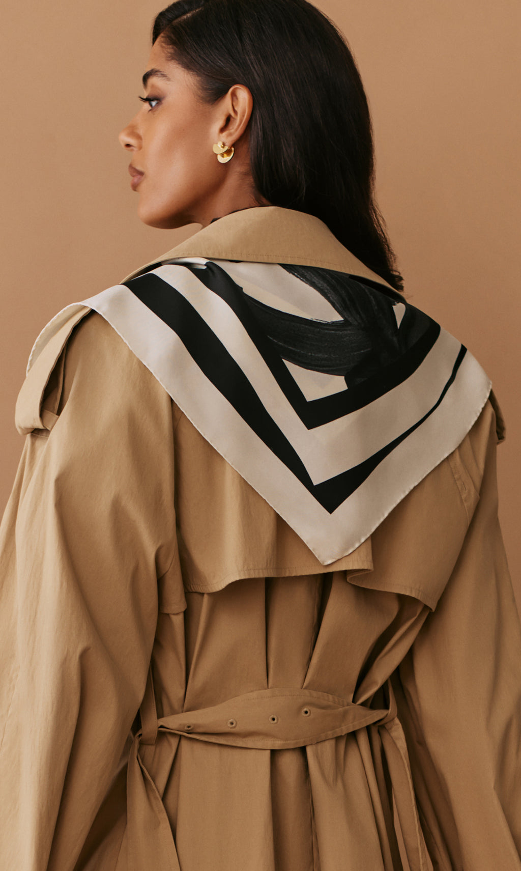 Person wearing a trench coat with a patterned scarf draped over the shoulders.