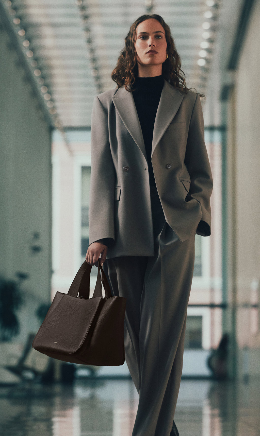 Person in suit walking indoors carrying a handbag