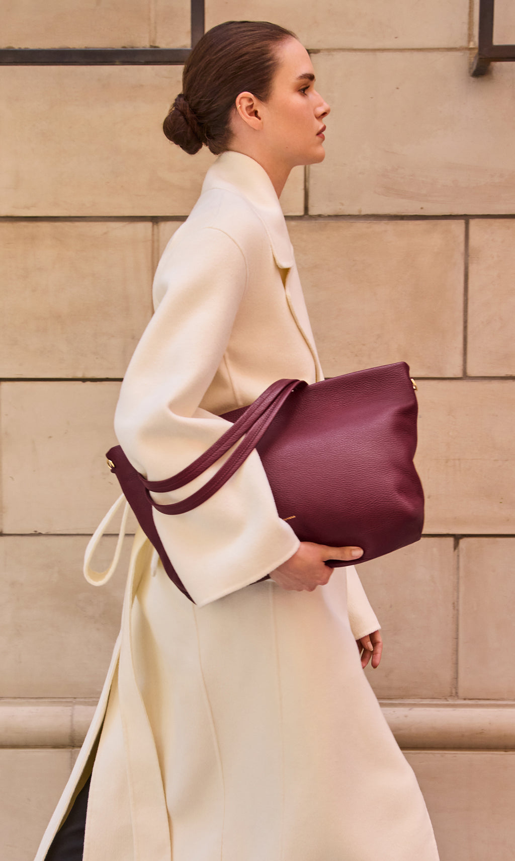 Person walking with a large shoulder bag wearing a long coat.