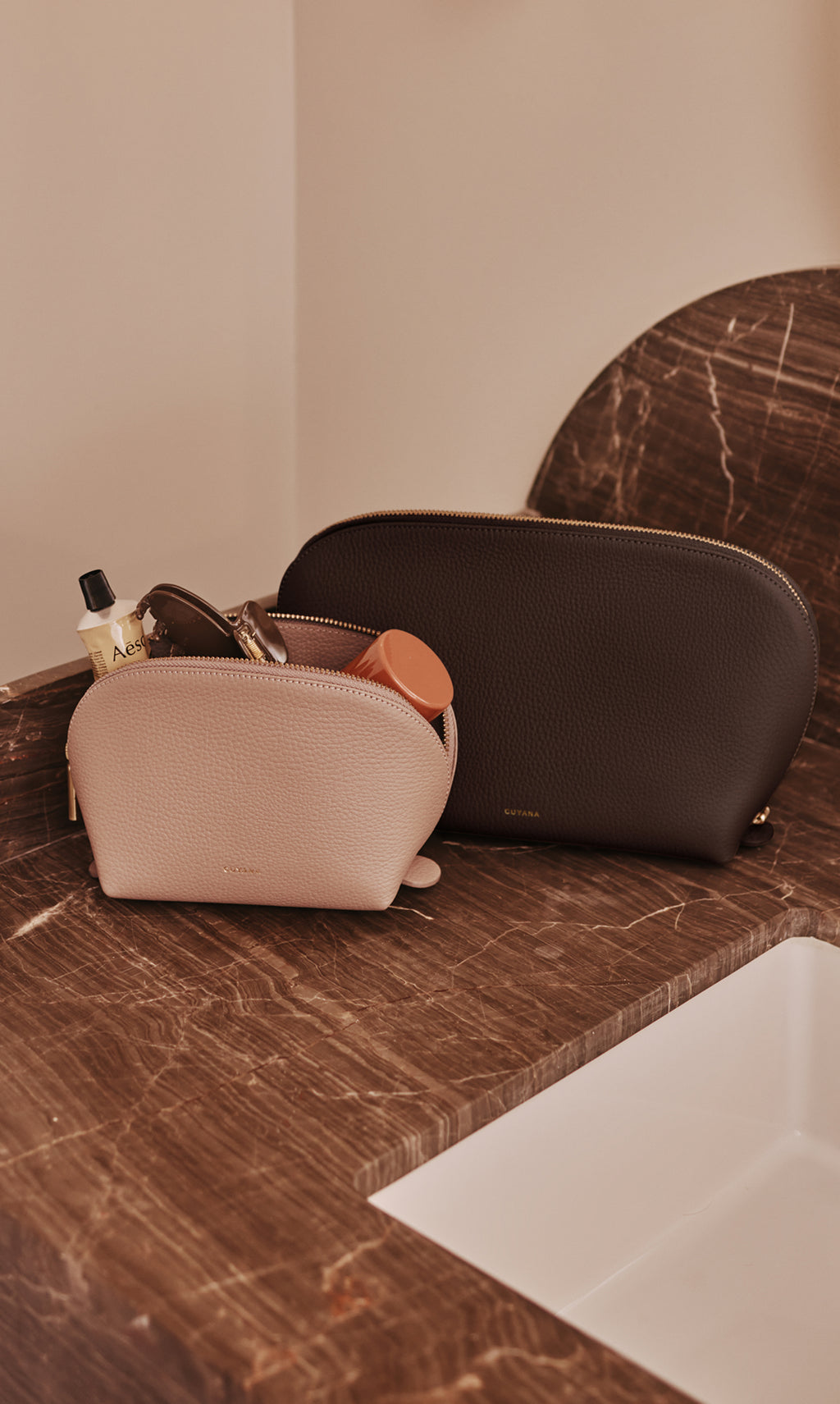 Two zippered pouches on a marble countertop next to a sink.