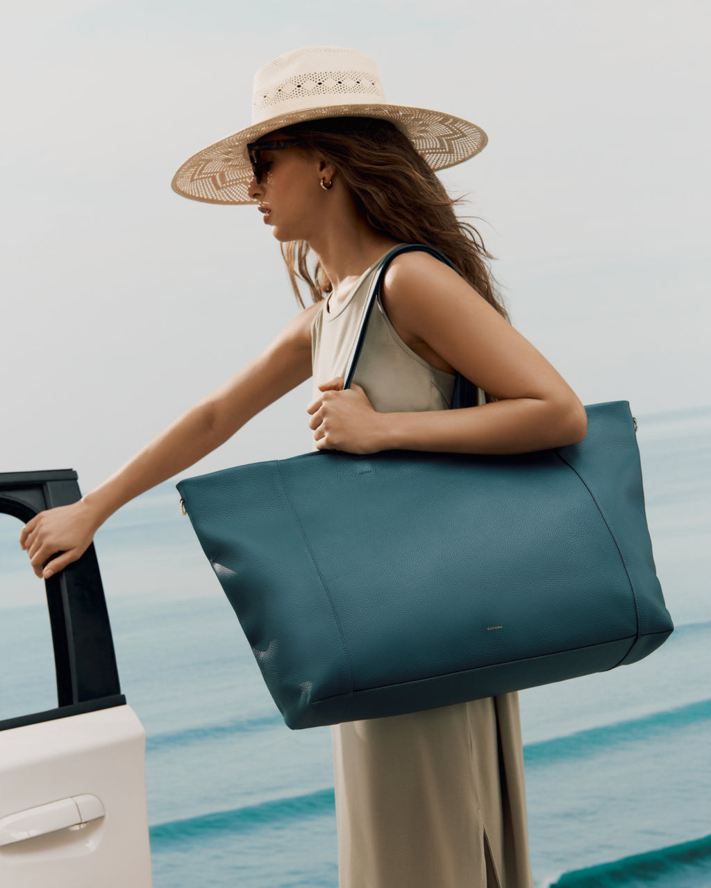 Woman carrying large tote bag next to car near a beach