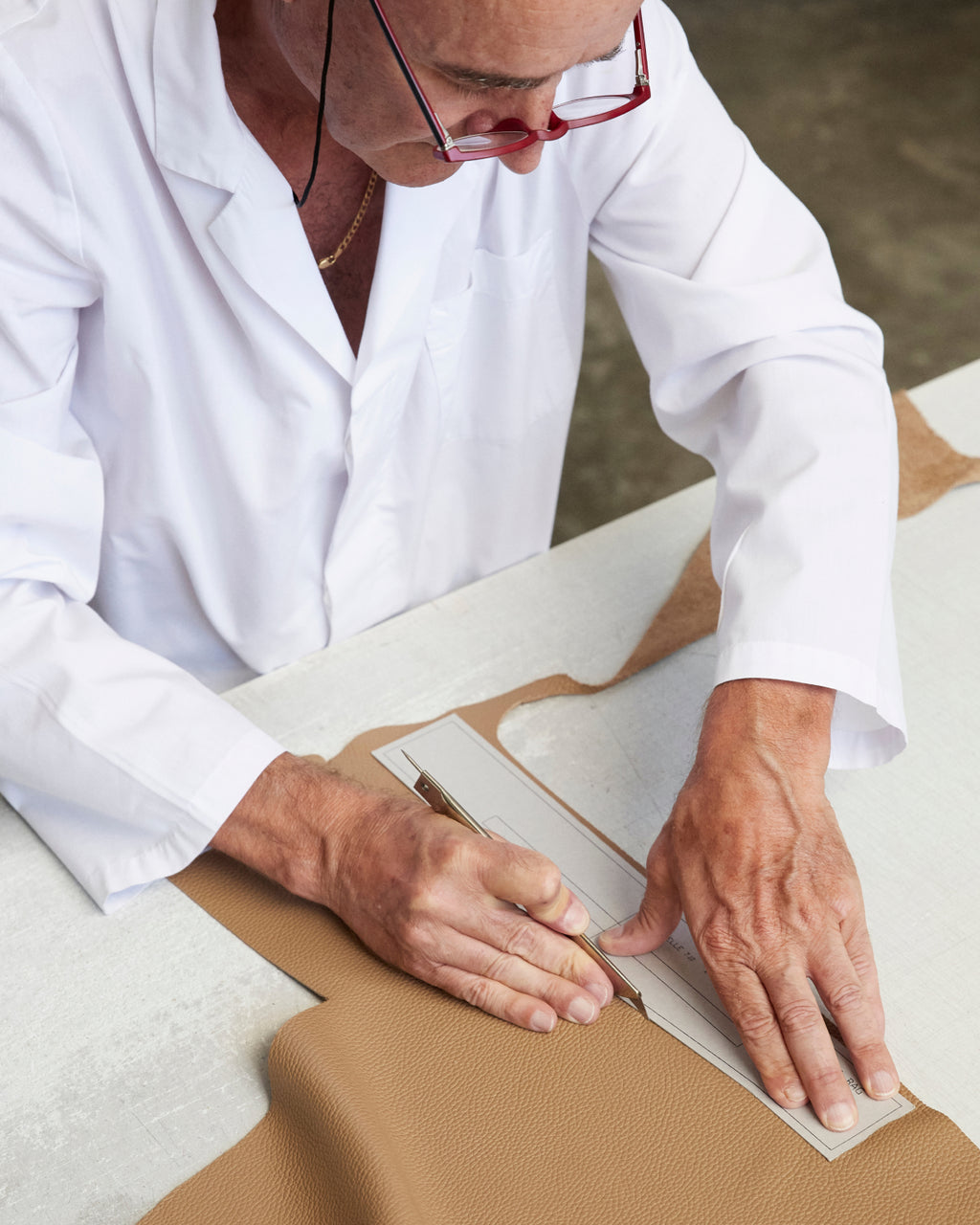 Person cutting a piece of leather with a ruler and knife.