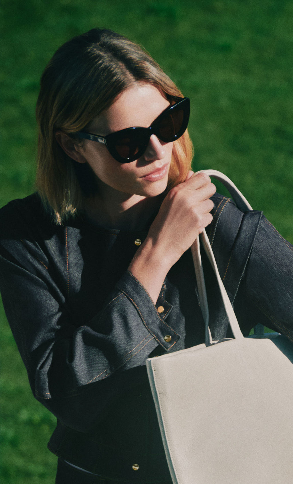 Person wearing sunglasses holding a tote bag outdoors.