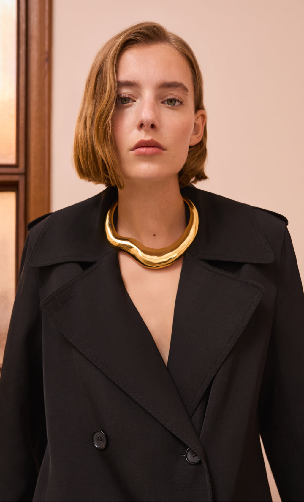 Person wearing a coat with large collar and chunky gold necklace.