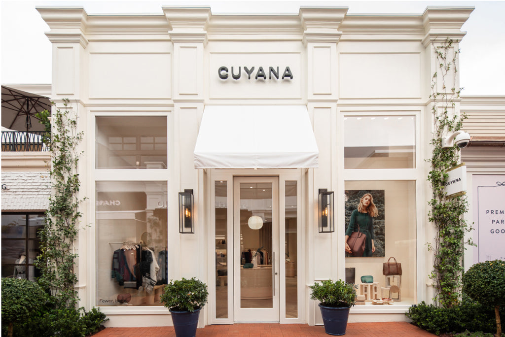 Front view of a Cuyana store with a mannequin and products visible through the windows.
