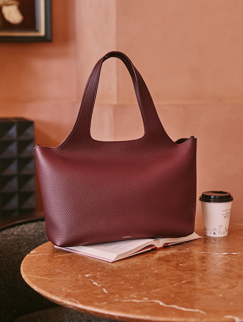 Handbag on a table with a book and a coffee cup nearby.