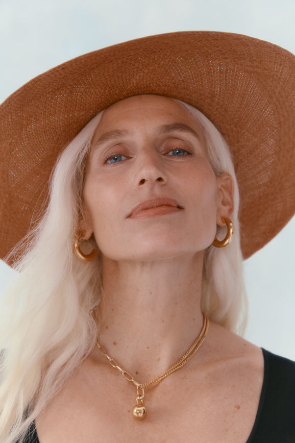 Woman wearing a wide-brimmed hat, earrings, and a necklace looking up.