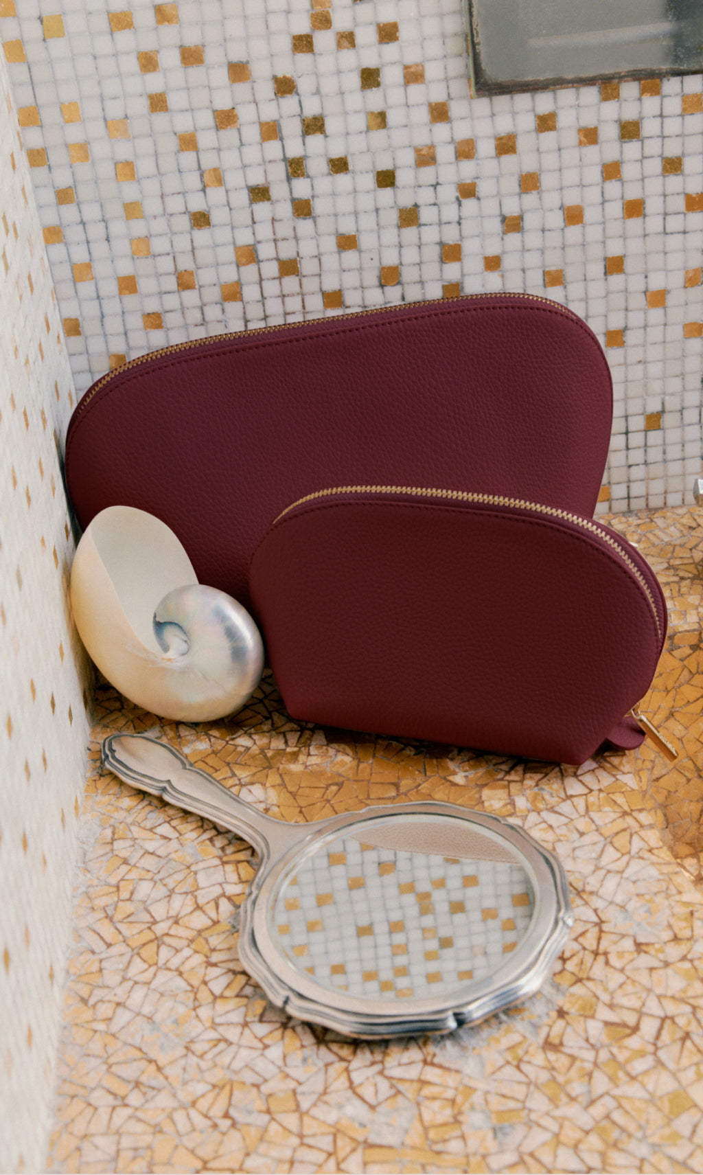 Two zippered pouches, a seashell, and a handheld mirror on a tiled surface.