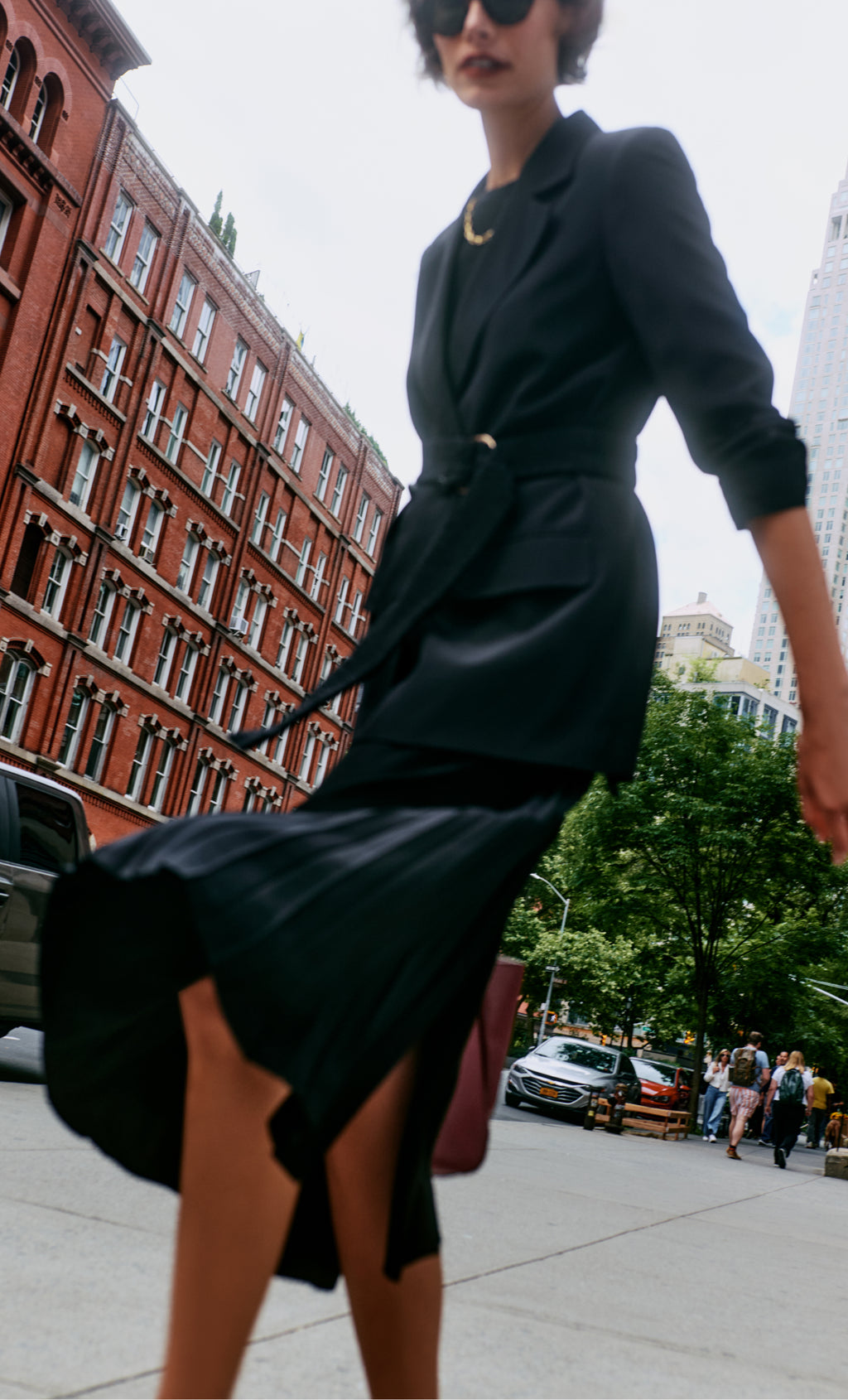 Person in a jacket and skirt walking on city sidewalk, with a tote bag.