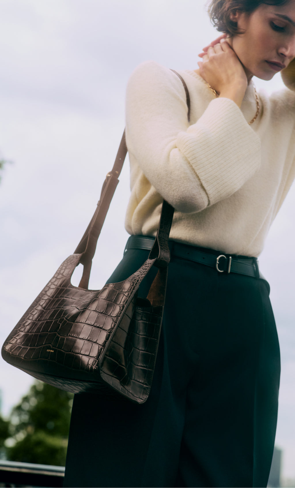 Person with croc-embossed leather handbag wearing a sweater and pants.