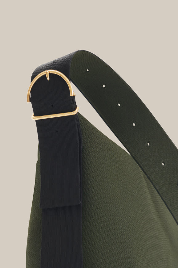 Close-up of a belt on a draped garment with metal buckle and adjustable holes.