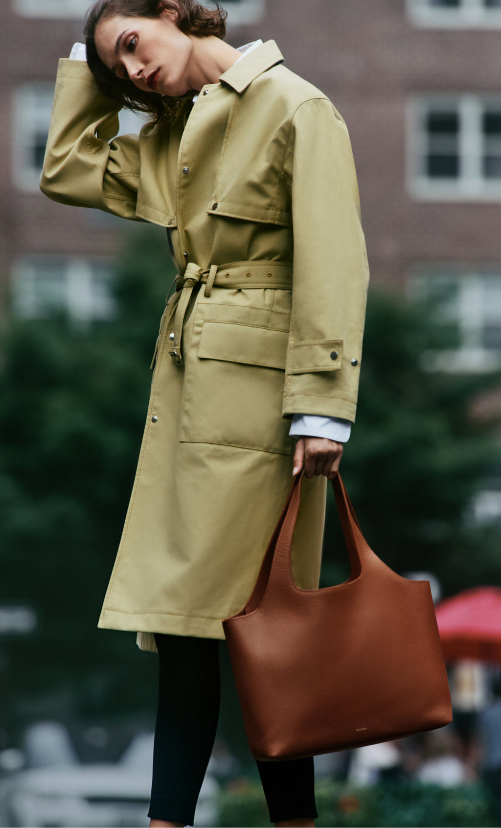 Person wearing a trench coat holding a brown tote bag