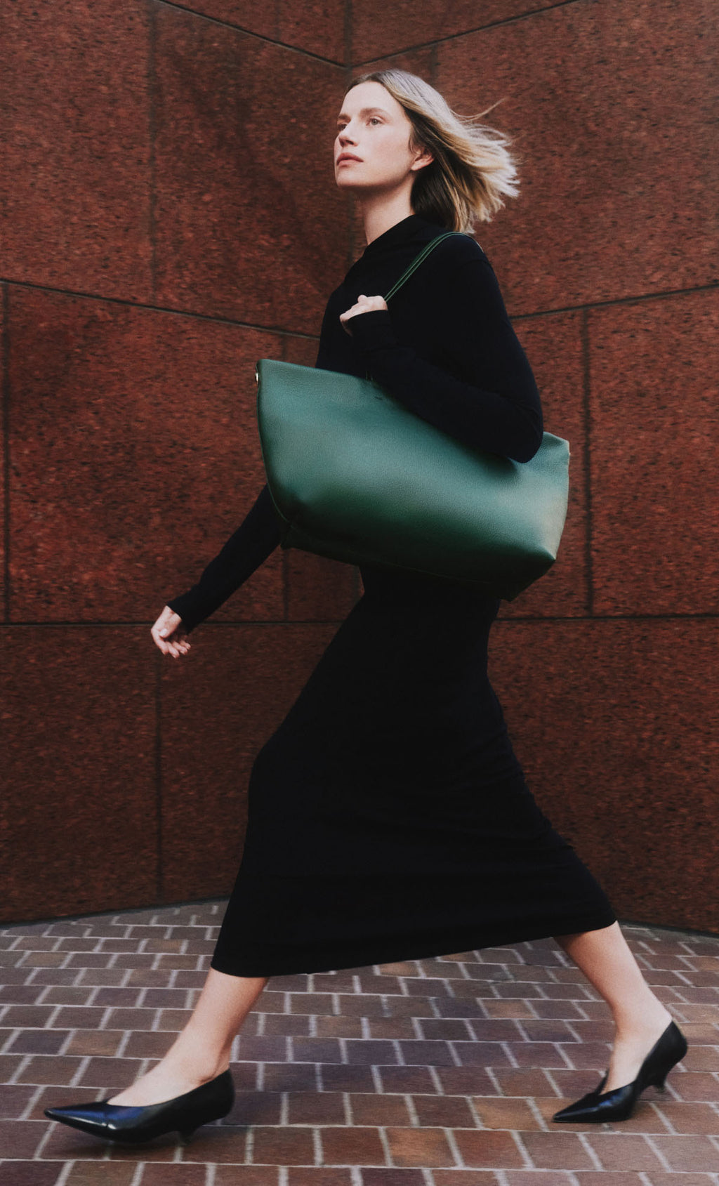 Person walking carrying a large shoulder bag against a brick wall background.