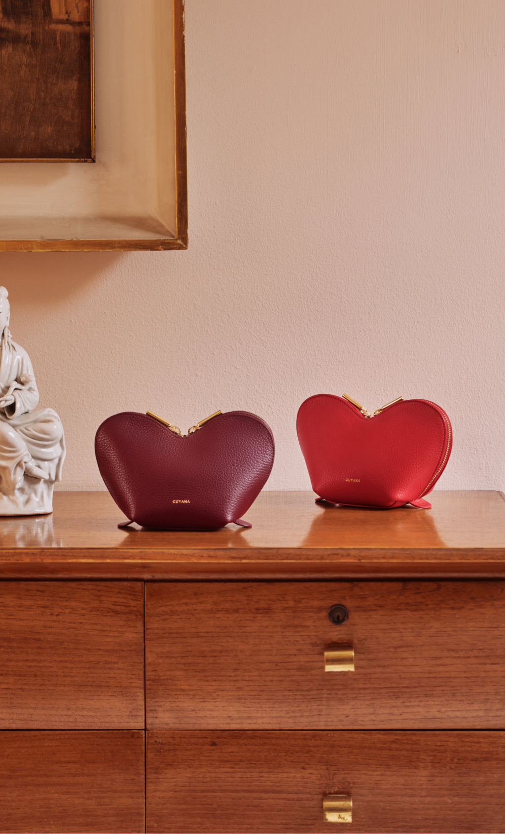 Two heart-shaped handbags on a wooden dresser.