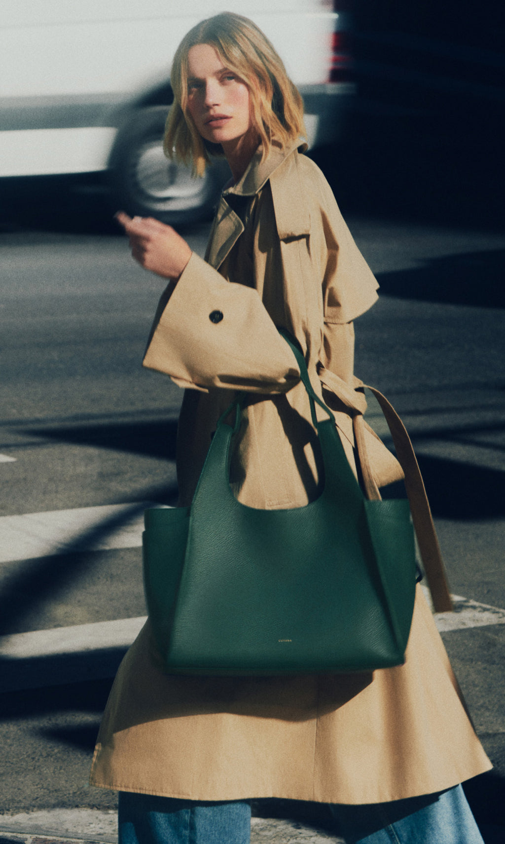 Person in a trench coat with a large shoulder bag walking on a street.