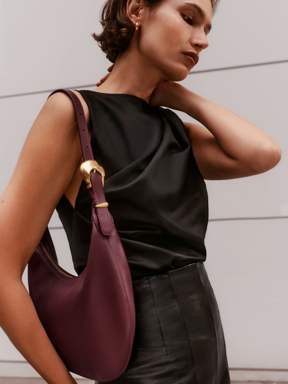 Person posing with handbag over shoulder, wearing sleeveless top and high-waisted trousers