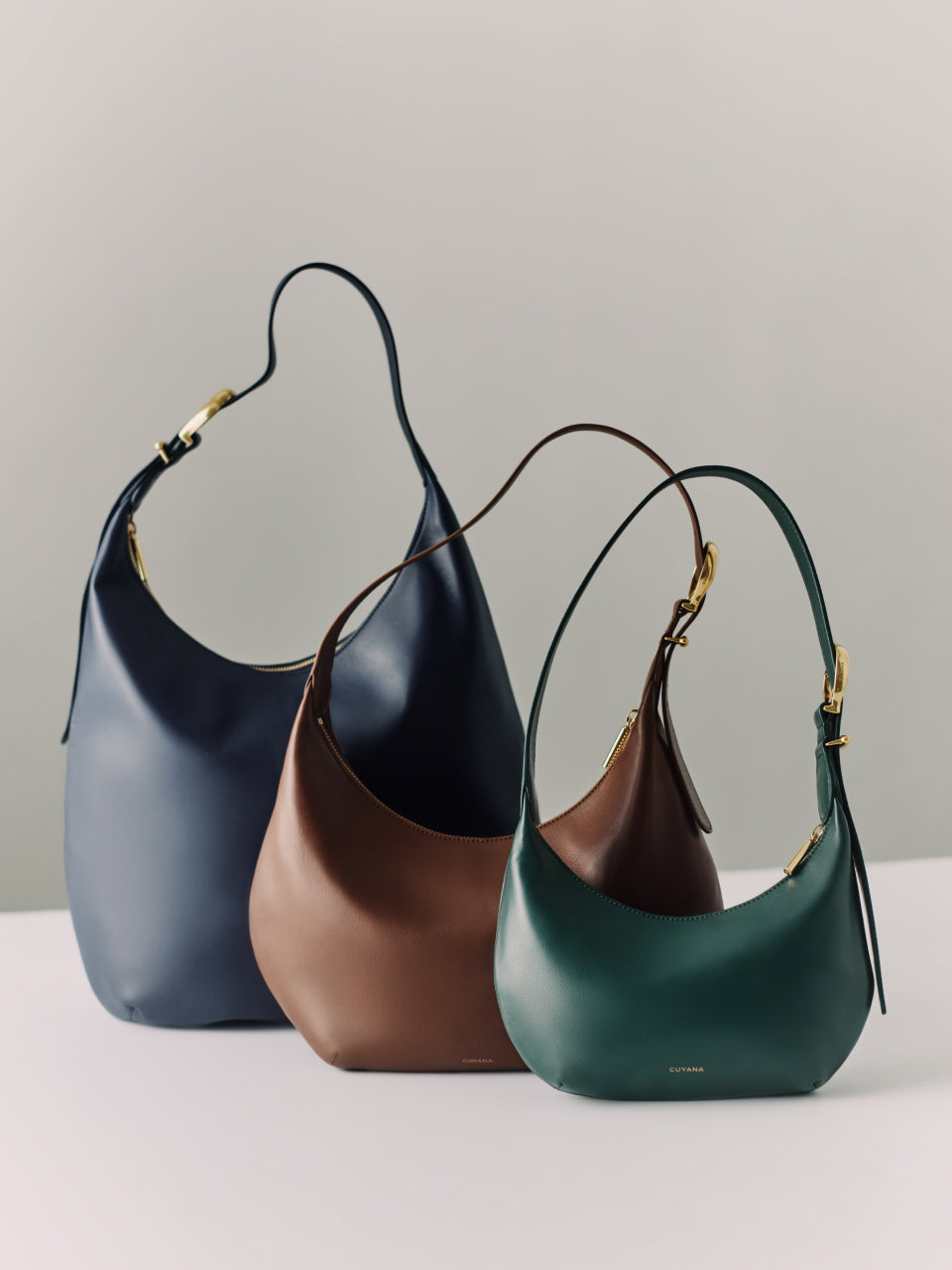 Three hobo bags with curved handles arranged on a flat surface.