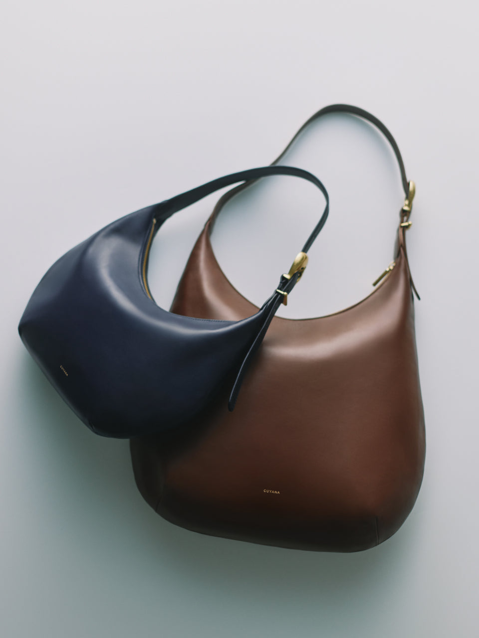 Two shoulder bags with curved shapes and metal buckles.