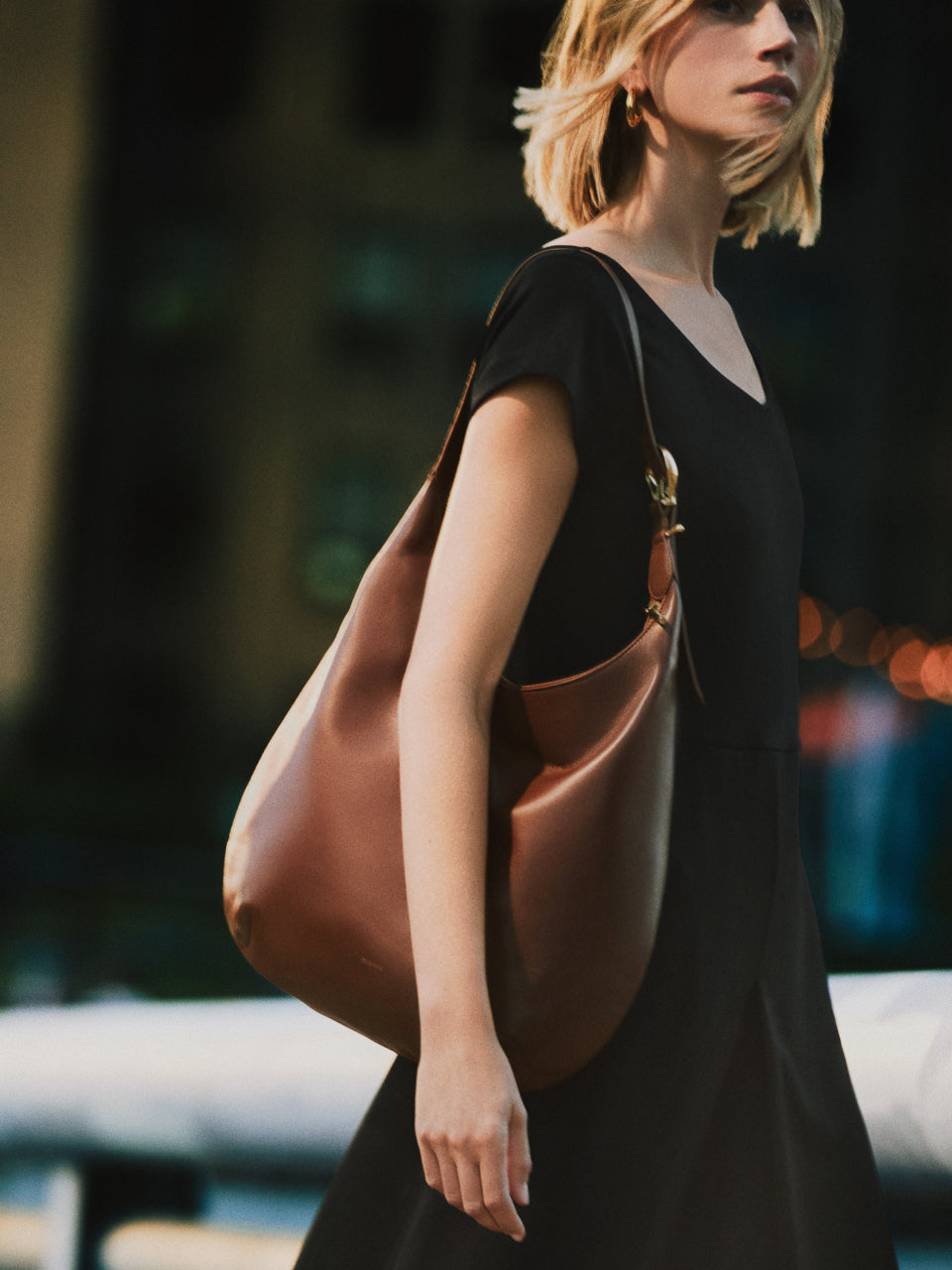 Person carrying a slouchy shoulder bag and wearing a dress in an urban setting.