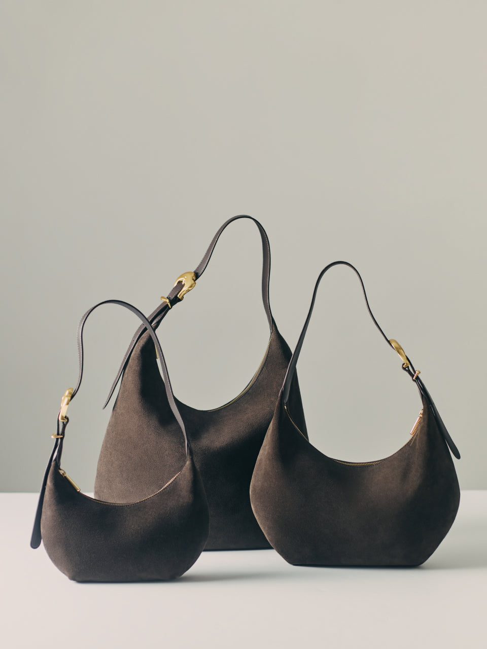 Three handbags with curved shapes and short handles.