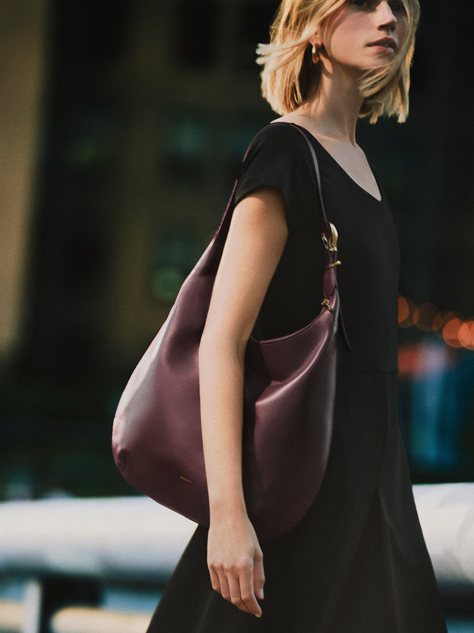 Person holding a large shoulder bag, standing outdoors in a city setting.