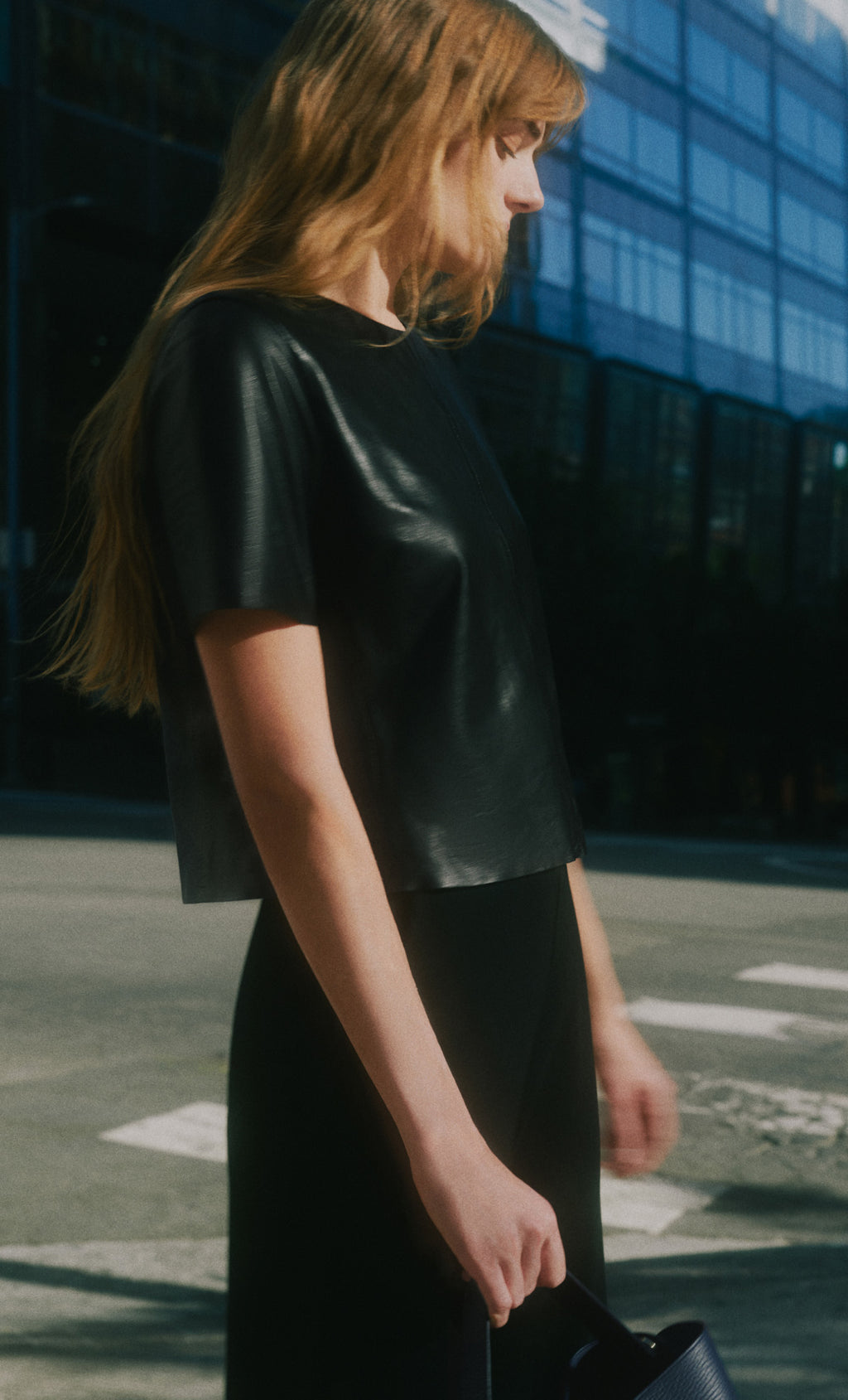 Person in dark top and skirt, holding a small bag, standing on a city street.