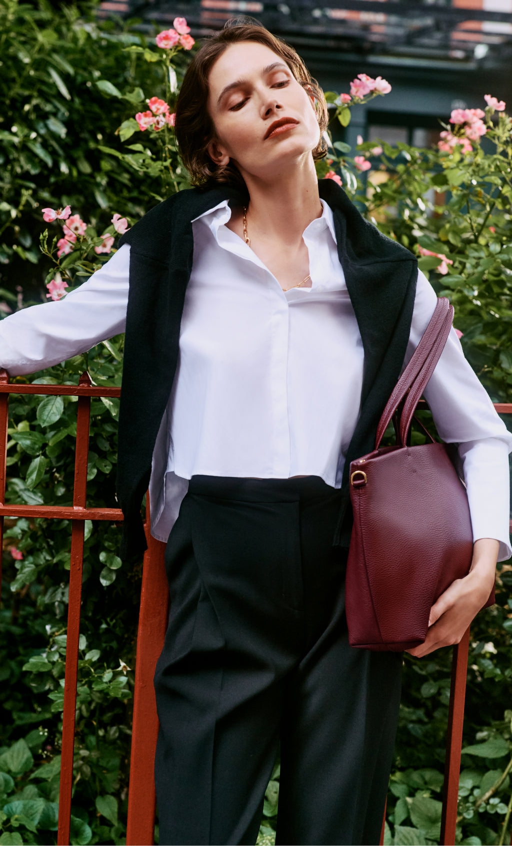 Person standing near a railing, wearing a shirt, pants, and holding a bag.