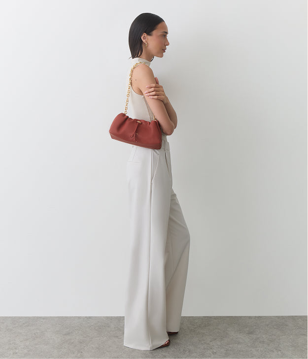 Person in sleeveless top and wide pants holding a small handbag over their shoulder.