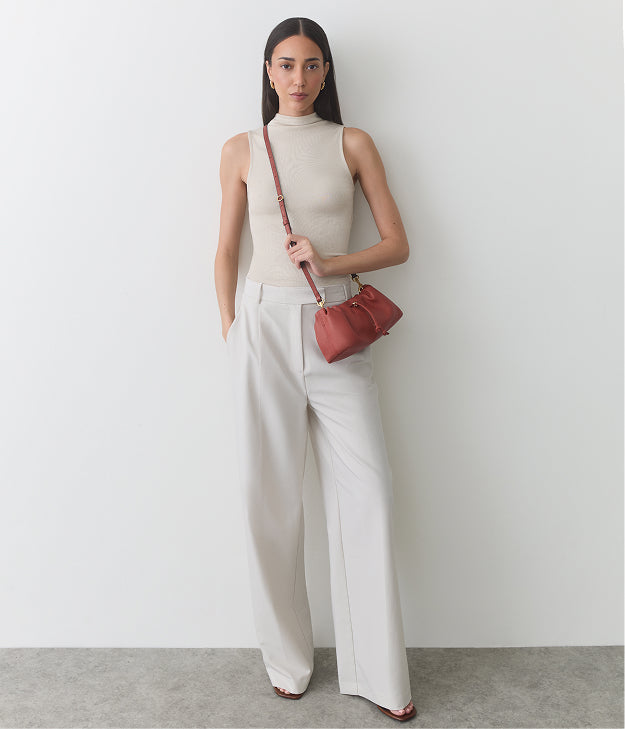 Person wearing sleeveless top and wide pants, holding small shoulder bag.