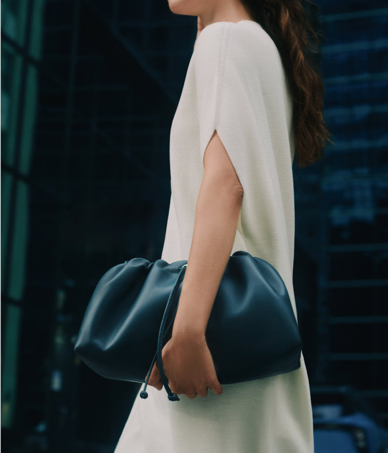 Person in a dress holding a large clutch bag in an urban setting.