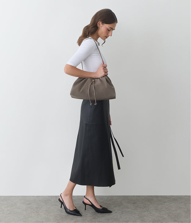 Person in profile with shoulder bag wearing a skirt and heels.