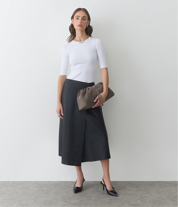 Person in a white top, black skirt, holding a clutch, and wearing heels.