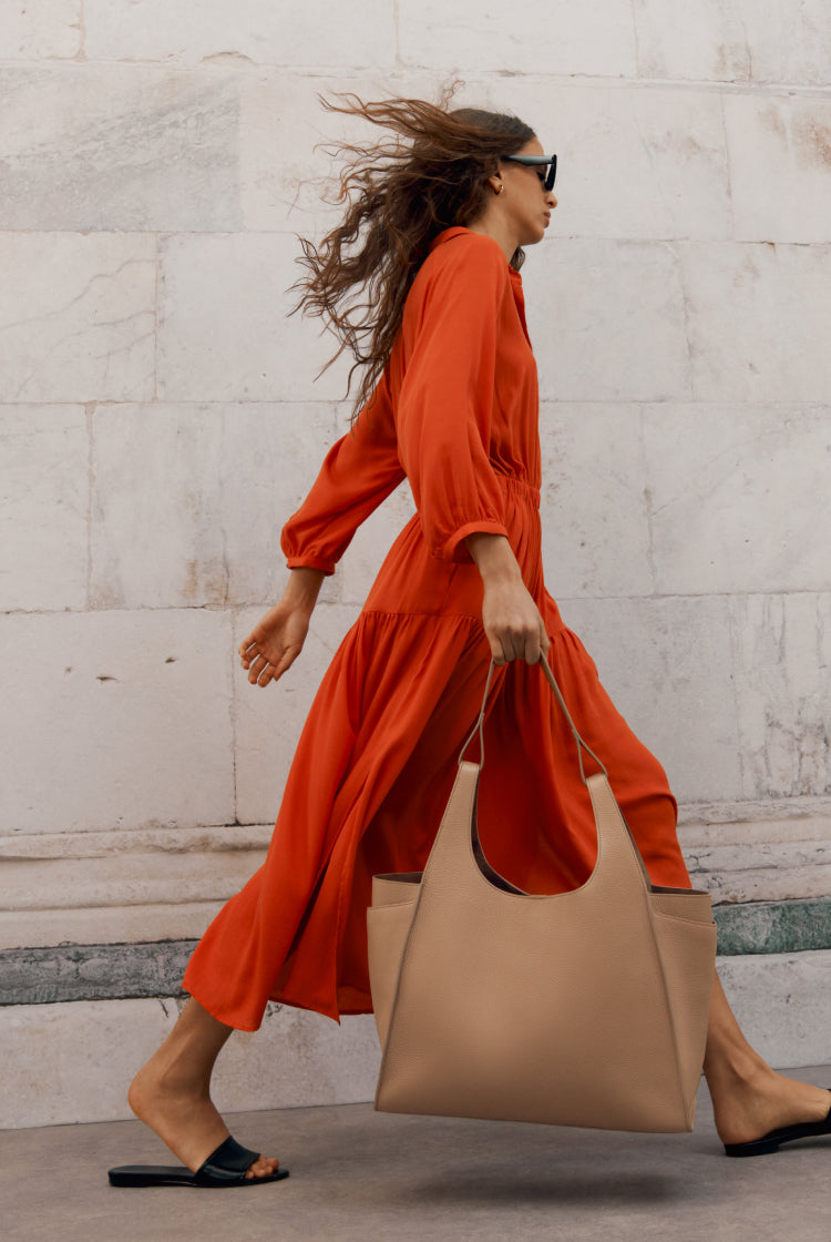 Woman walking briskly, carrying a large bag and wearing sunglasses.