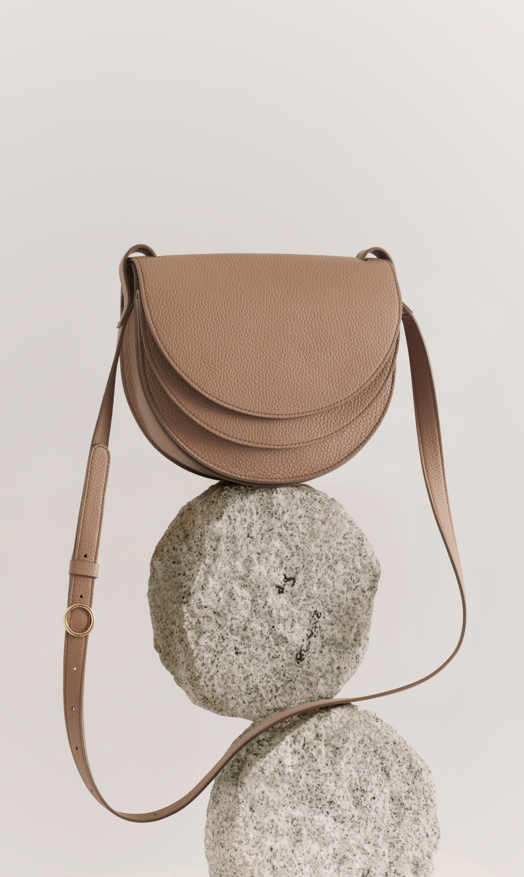 Curved crossbody bag with a strap, displayed on two round stones.