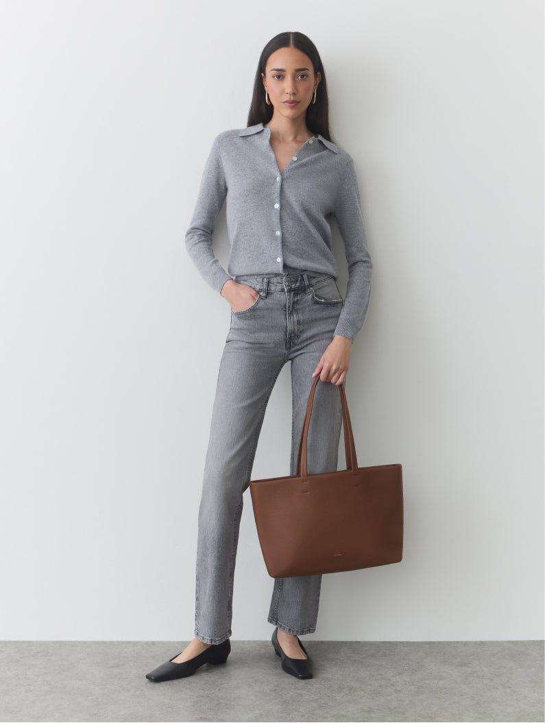Person standing, wearing a shirt and jeans, holding a large tote bag.