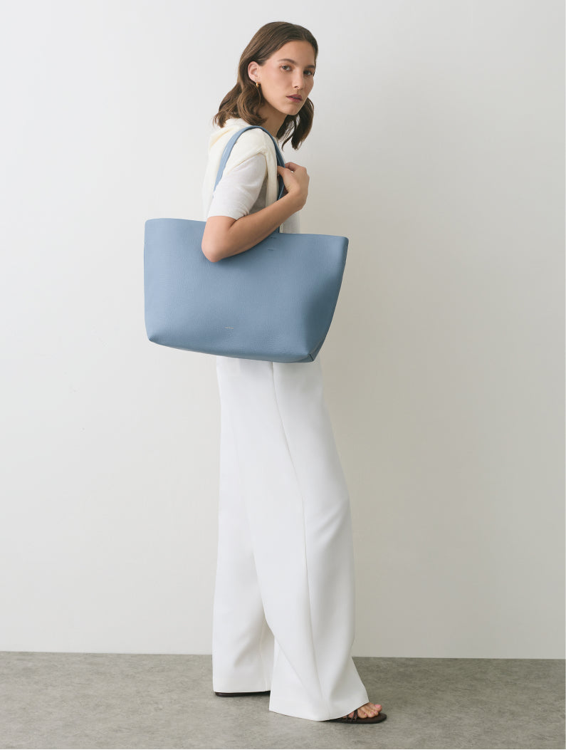 Person standing with large shoulder bag in minimalist outfit.