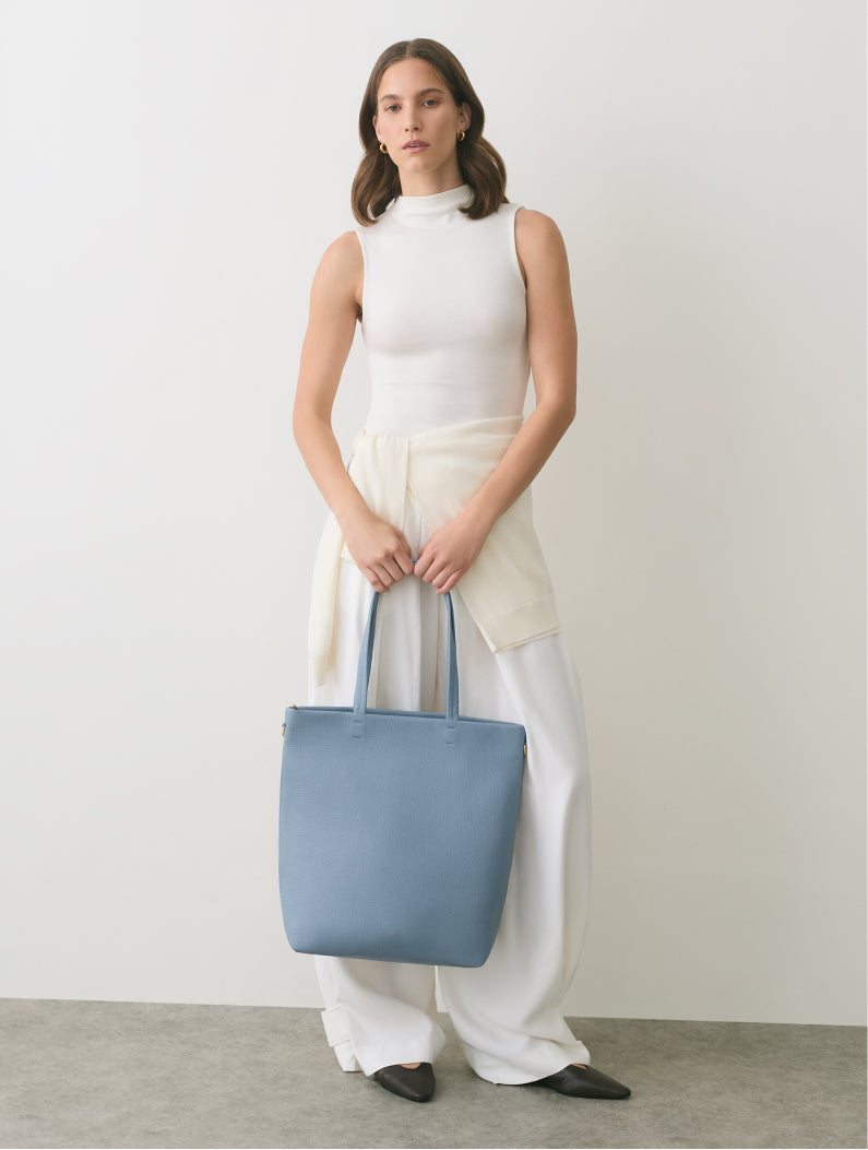 Person holding a tote bag, wearing a sleeveless top and wide-leg pants.