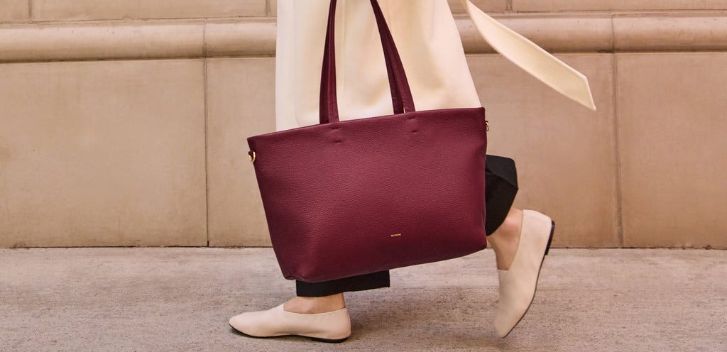 Person walking with large handbag and wearing flats along a sidewalk.