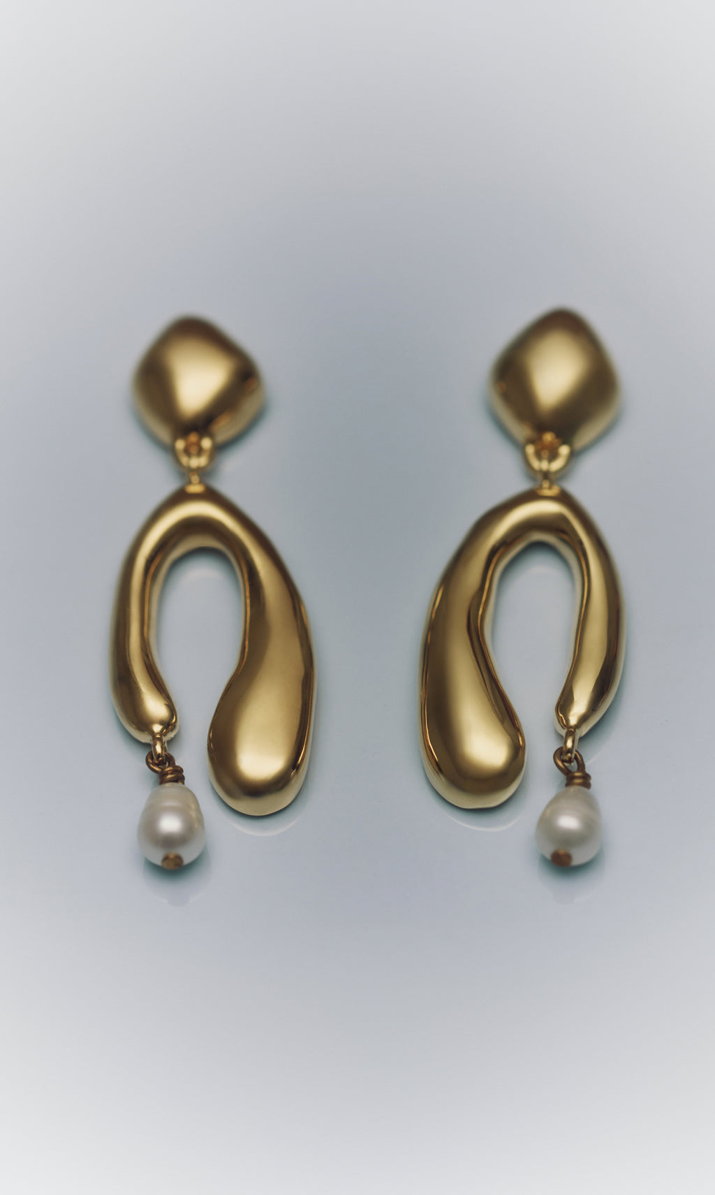 Pair of abstract gold earrings with pearls hanging below.