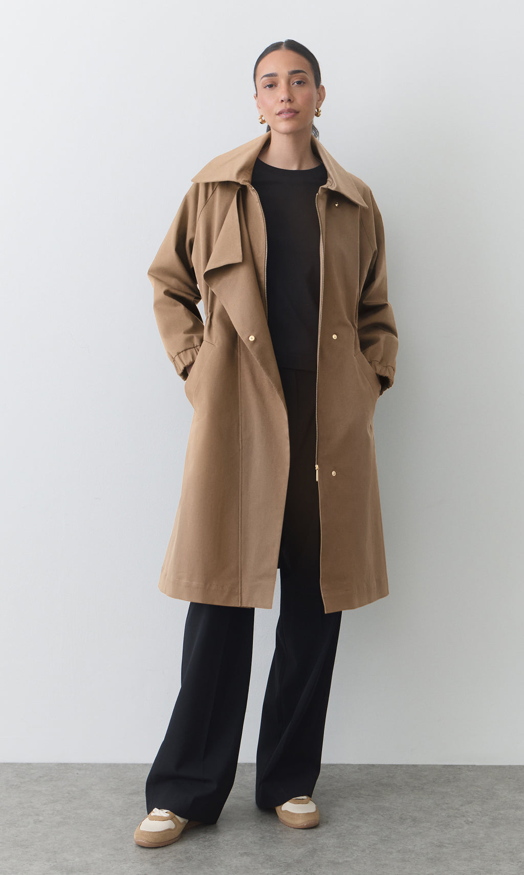 Person wearing a long coat, top, pants, and loafers standing against a plain background.